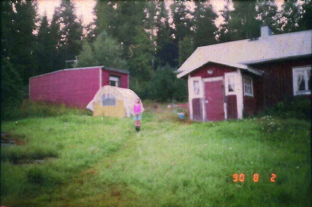 Photograph from the series Behind the Looking Glass by Anna Wiksten: a child in front of a house and a tent, scanned in negative from the 1990's.