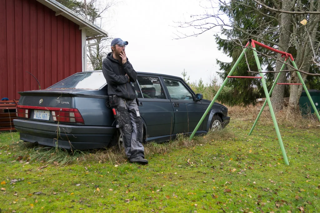 Fotografi ur serien Människor och miljö av Anna Wiksten: rökande man framför bil.