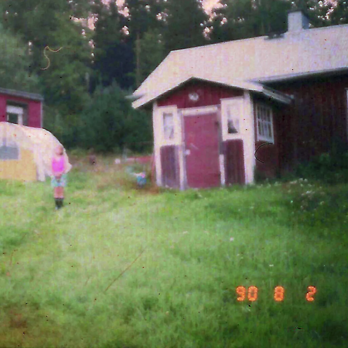 Fotografi ur serien Memory Starts Here av Anna Wiksten: barn framför hus och tält, inskannat negativ från 1990-talet.